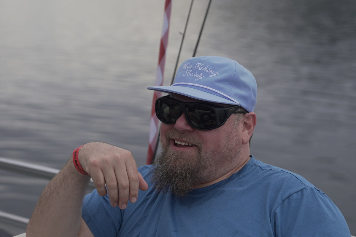 Light blue Slow Fishing Society script hat worn on a boat